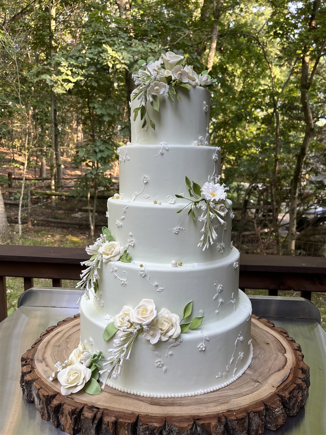Five-tier wedding cake with sugar roses and blossoms on a wood slab