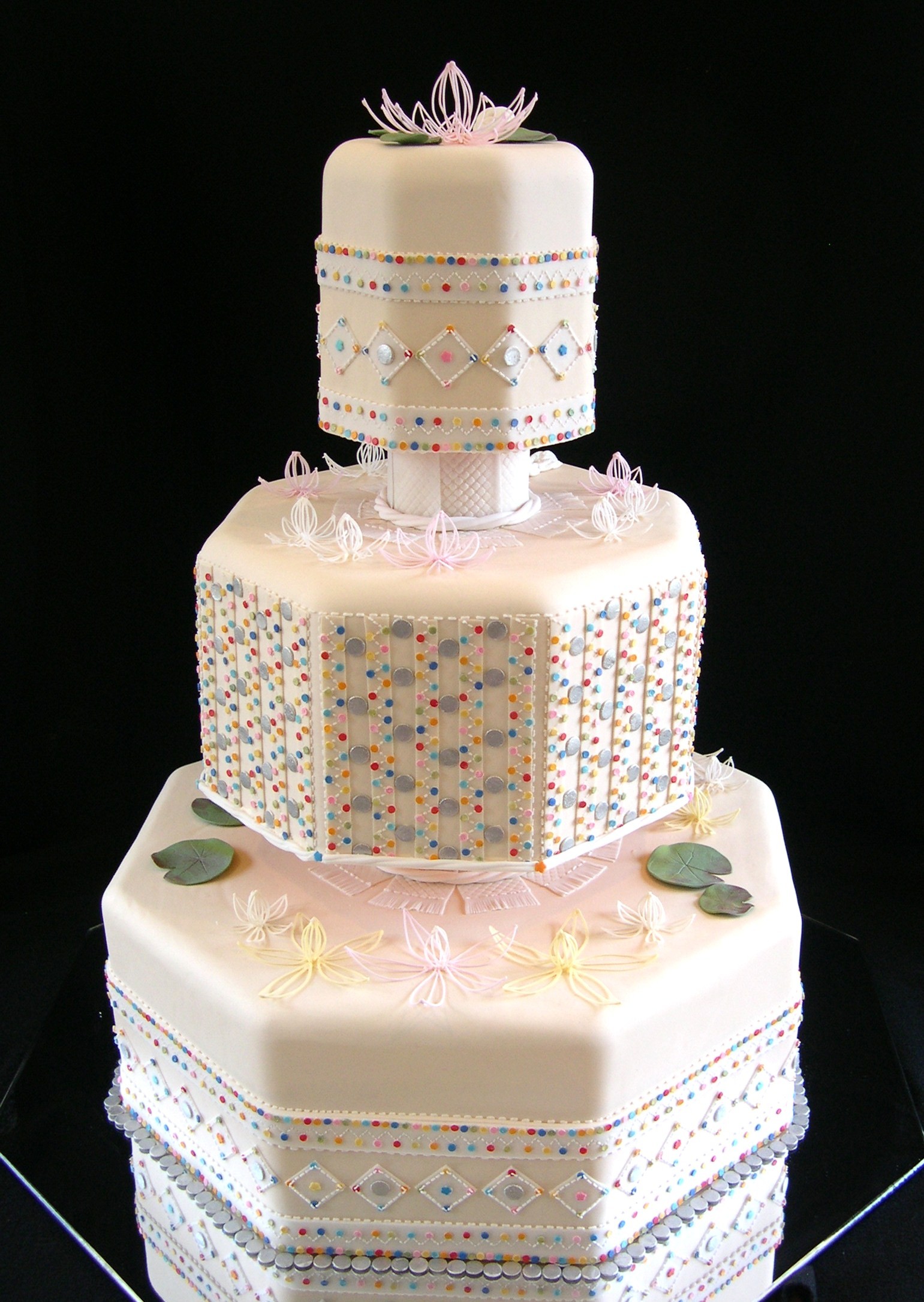 Three-tier octagonal wedding cake with piped lotus flowers and colorful dots